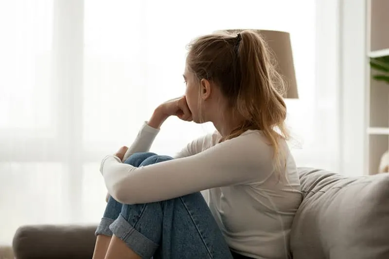 traurige junge Frau, die auf Sofa sitzt und denkt