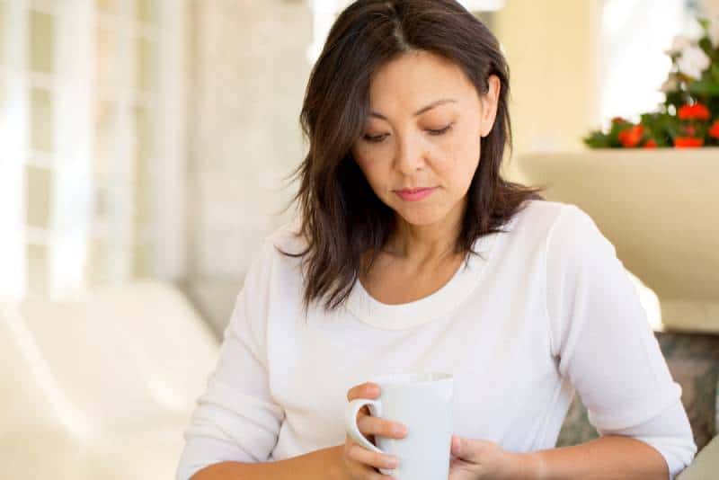 traurige reife Frau, die zu Hause sitzt und Tasse hält