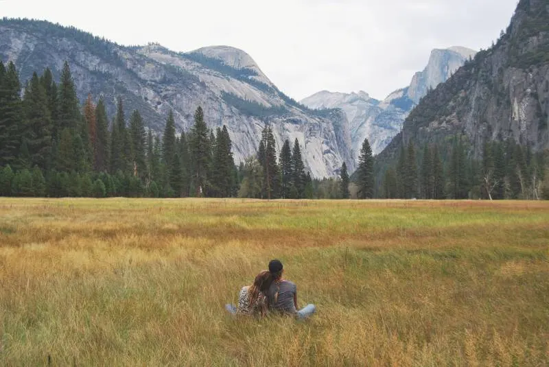 zwei Personen, die im Grasfeld sitzen und Berg betrachten