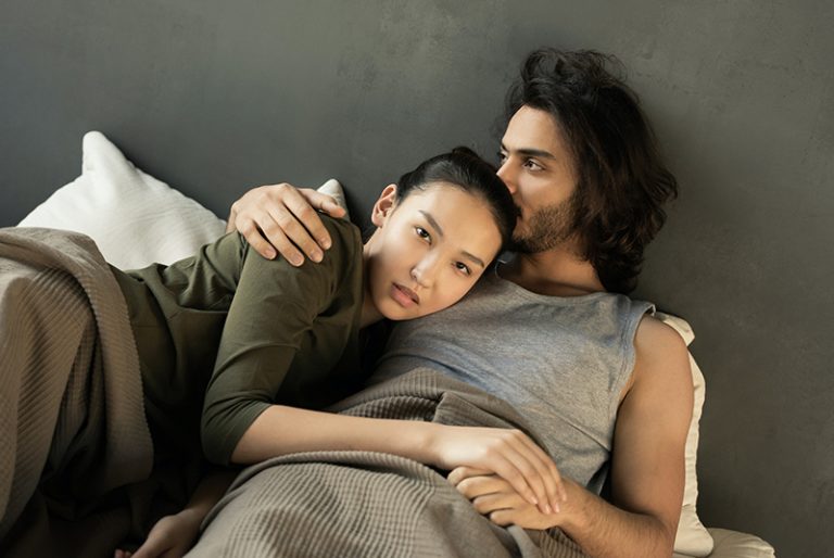 eine ernsthafte Frau, die sich auf einen Mann im Bett stützte