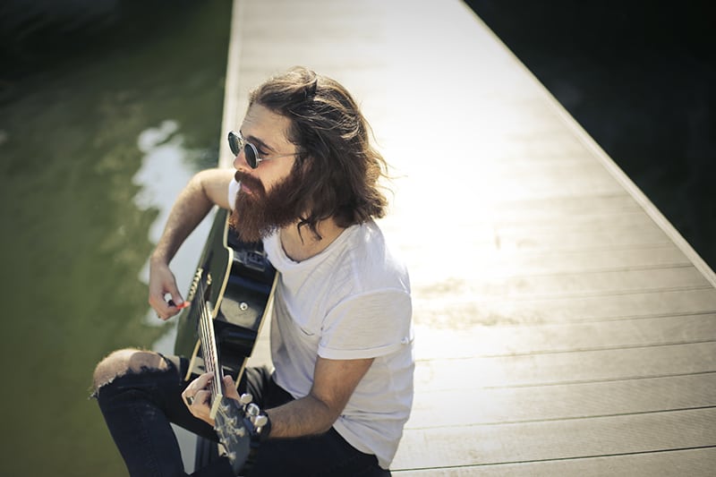 Ein Mann, der Gitarre spielt, während er Zeit alleine am See verbringt