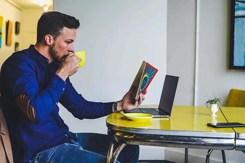 Ein Mann, der ein Buch liest und Kaffee trinkt, bemerkt nicht, dass ein Smartphone auf dem Tisch piept