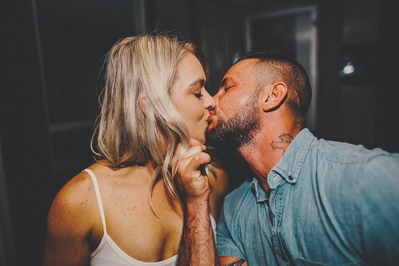 Ein Mann in einem blauen Hemd küsst eine Frau mit blonden Haaren und trägt ein weißes Oberteil