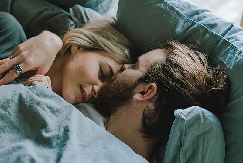 Ein Mann küsst eine Frau auf die Stirn, während sie im Bett schläft