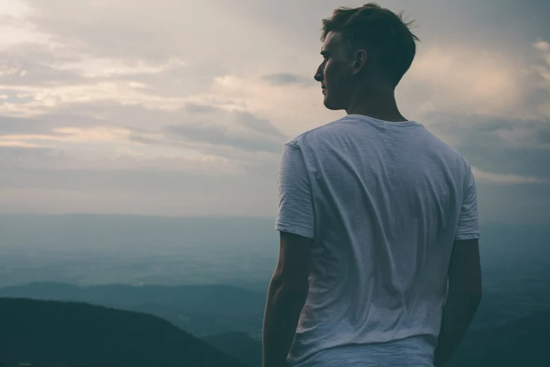Ein Mann steht auf der Klippe mit Blick auf die Berge und beobachtet den Sonnenuntergang