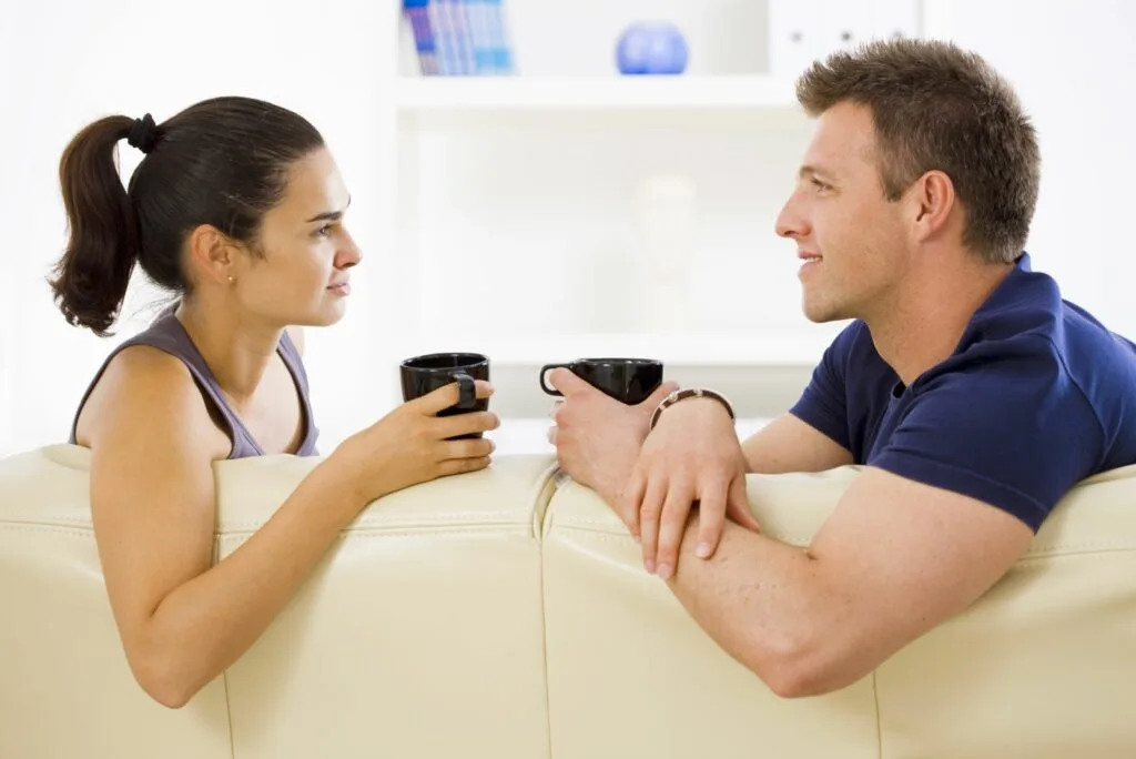 Ein Mann und eine Frau sitzen auf einer Couch und halten Tassen in den Haenden