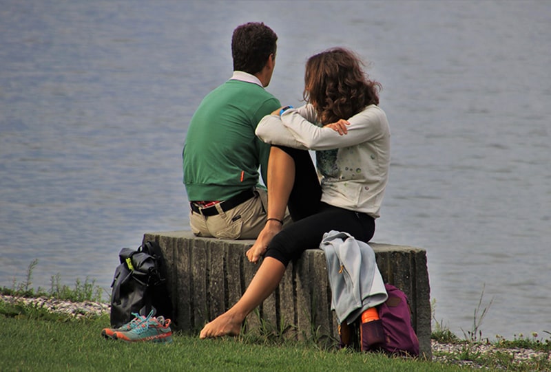 Ein Mann und eine Frau sitzen neben dem Gewässer auf der Betonbank