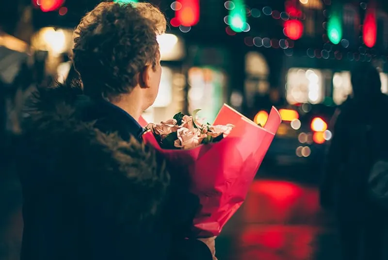 Ein Mann wartet auf seine Freundin und hält einen Blumenstrauß