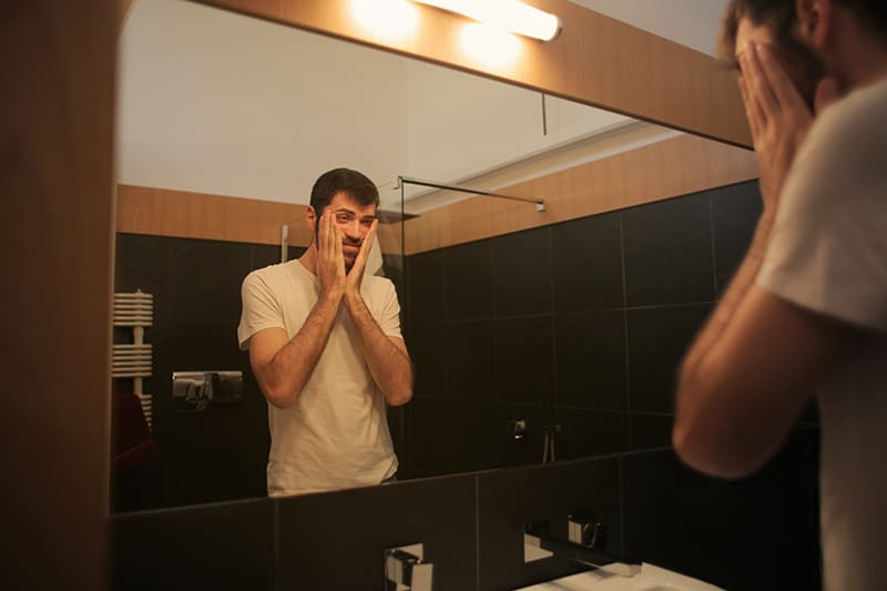 Ein nervöser Mann stand vor dem Spiegel und berührte das Gesicht