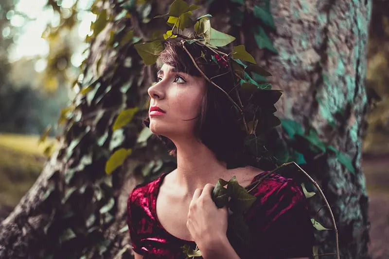 Eine Frau mit einem Kranz im Haar steht neben einem Baum und wartet auf jemanden