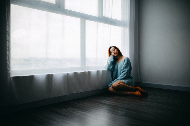 Eine traurige Frau sitzt auf dem Boden am Fenster