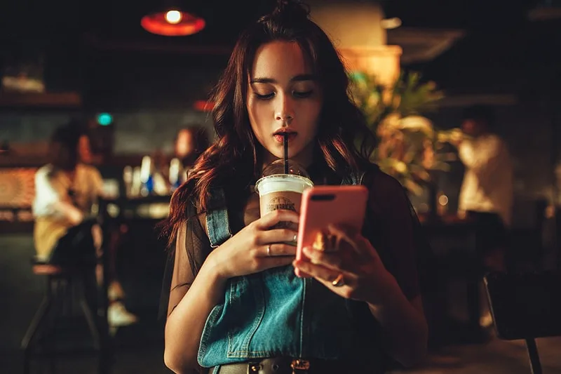 Eine Frau überprüft ihr Telefon, während sie Kaffee trinkt