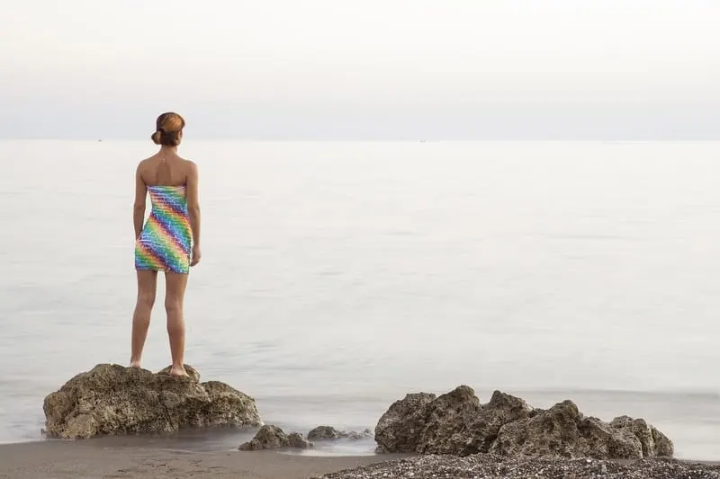 Frau steht auf Stein und schaut auf das Meer