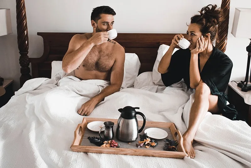  Frau und Mann sitzen auf dem Bett beim Kaffeetrinken
