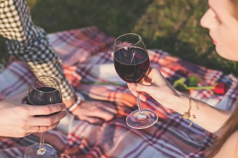 Liebespaar, das Wein auf einem Picknick trinkt, während es auf der Decke sitzt