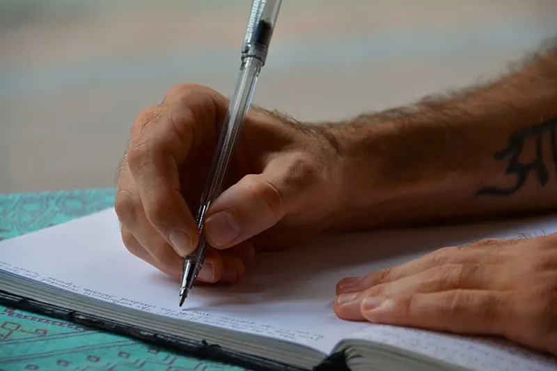 Mann Schreiben in Notizbuch auf blauer Oberfläche