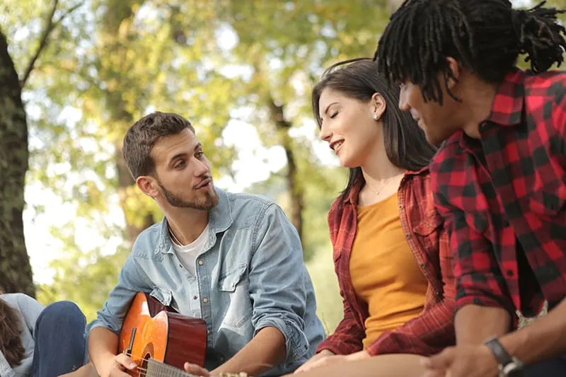  Mann mit Gitarre, die zu Freunden singt, während er Mädchen ansieht
