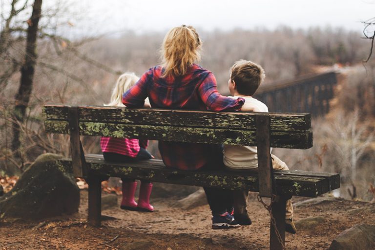 eine Mutter und zwei Kinder sitzen auf der Bank in der Natur