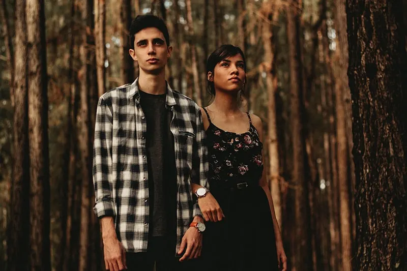 Ein ernster Mann und eine ernsthafte Frau stehen im Wald und halten sich an den Händen