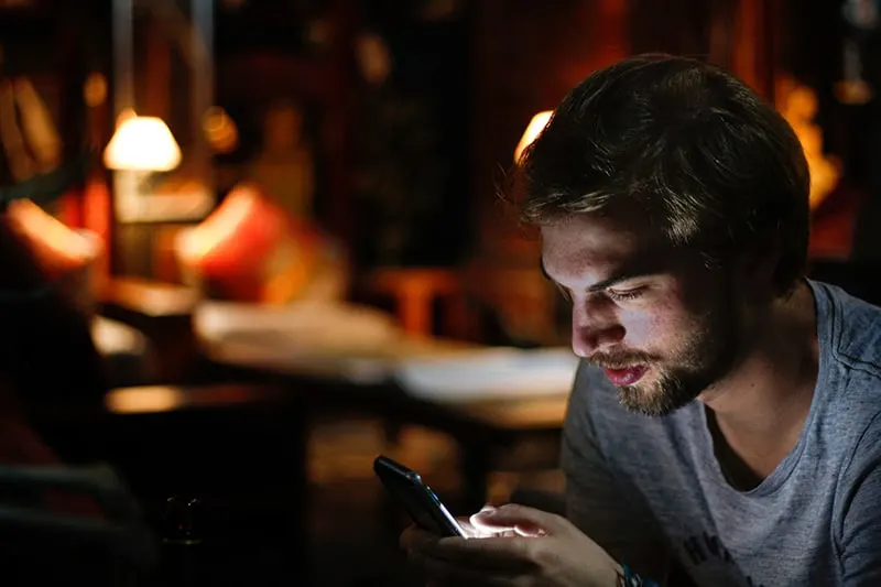 Ein Mann liest eine Nachricht auf einem Smartphone und sitzt in der Dunkelkammer
