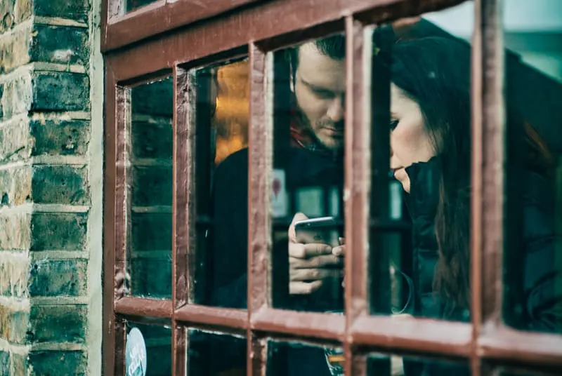 Ein Mann benutzt ein Smartphone neben einer Frau, während er in der Nähe des Fensters steht
