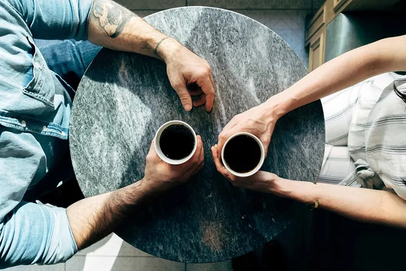 Ein Mann und eine Frau halten eine Kaffeetasse, während sie am Tisch sitzen