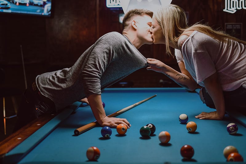 Ein Mann und eine Frau küssen sich auf dem Billardtisch