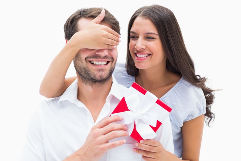 ein Mädchen, das einen Freund mit einem Geschenk zum Jubiläum überrascht