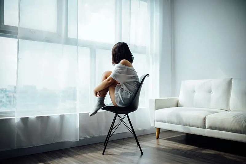 eine Frau, die alleine neben dem Fenster auf dem Stuhl sitzt