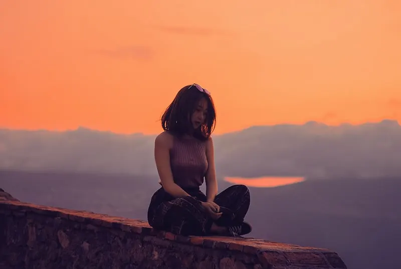 eine Frau, die allein auf einer Betonwand während des Sonnenuntergangs sitzt
