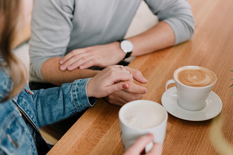 eine Frau, die die Hand eines Mannes hält, während sie im Café einen Kaffee trinkt