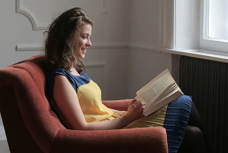 eine Frau, die ein Buch liest, während sie in der Nähe des Fensters sitzt