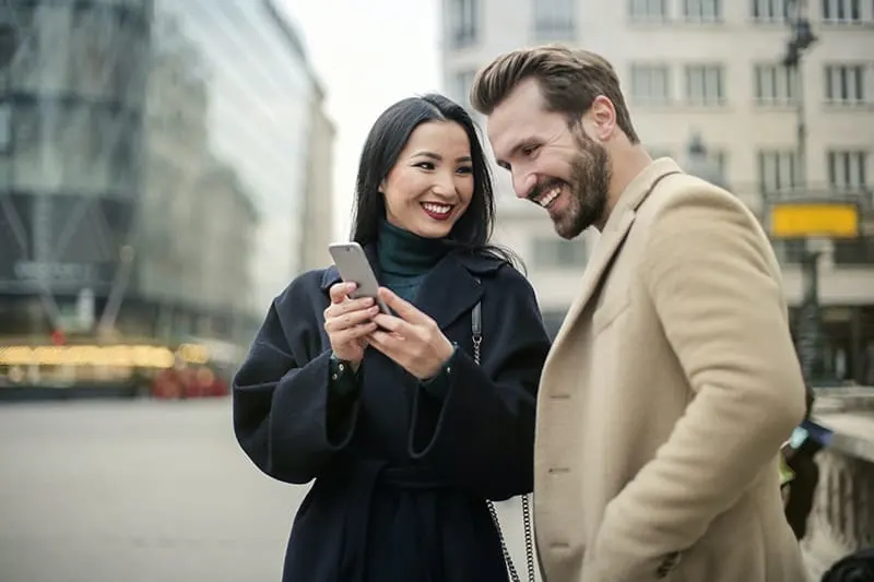 eine Frau, die einem Mann etwas auf einem Smartphone zeigt, während sie in der Stadt steht