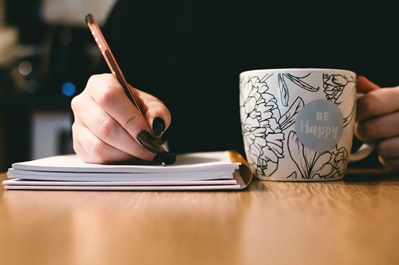eine Frau, die einen Abschiedsbrief schreibt, während sie eine Tasse am Tisch hält