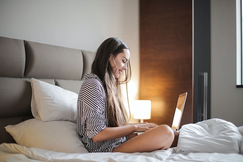 eine Frau, die einen Videoanruf auf dem Laptop hat, während sie auf dem Bett sitzt