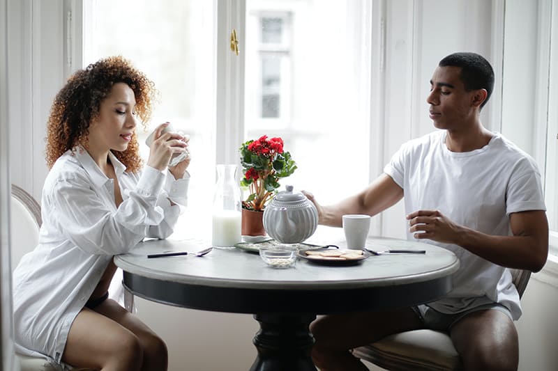 eine Frau, die in Kaffee starrt, während sie neben einem Mann sitzt während des Frühstücks