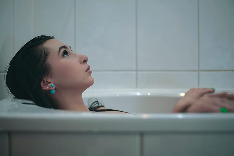 eine Frau, die mit Gedanken kämpft, während sie in der Badewanne liegt