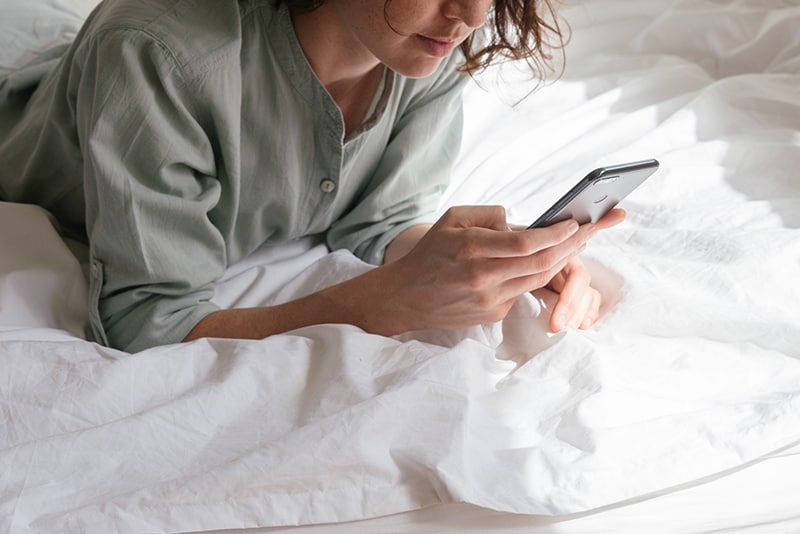 eine Frau, die mit einem Smartphone für einen Videoanruf auf dem Bett liegt