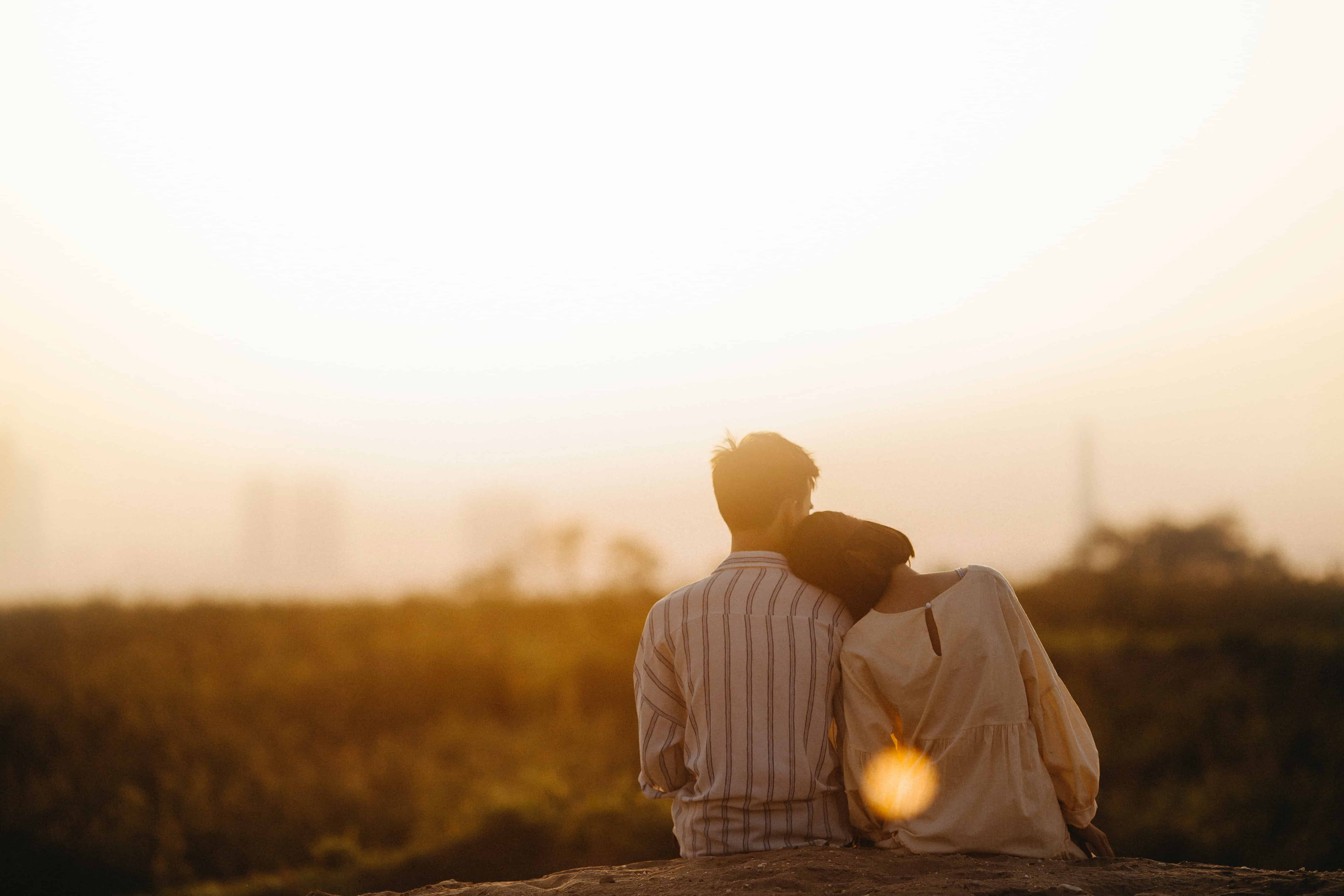 eine Frau, die sich auf einen Mann stützt, während sie während des Sonnenuntergangs in der Natur sitzt