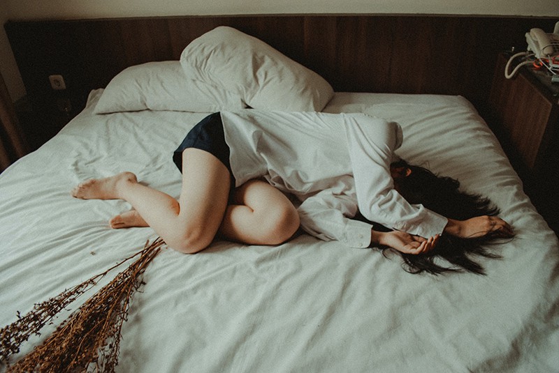 eine Frau im Gefühlschaos, die auf dem Bett liegt und ihren Kopf verstecken