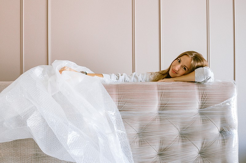 eine Frau, die mit einem Lächeln im Gesicht ein neues Kopfteil fürs Bett auspackt