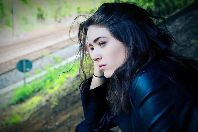 eine nachdenkliche Frau, die beiseite schaut, während sie in der Nähe der Eisenbahn sitzt