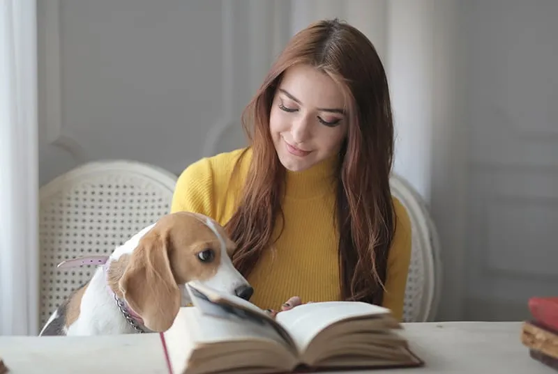 eine positive Frau, die den Hund ansieht, während sie mit Buch vor ihr sitzt