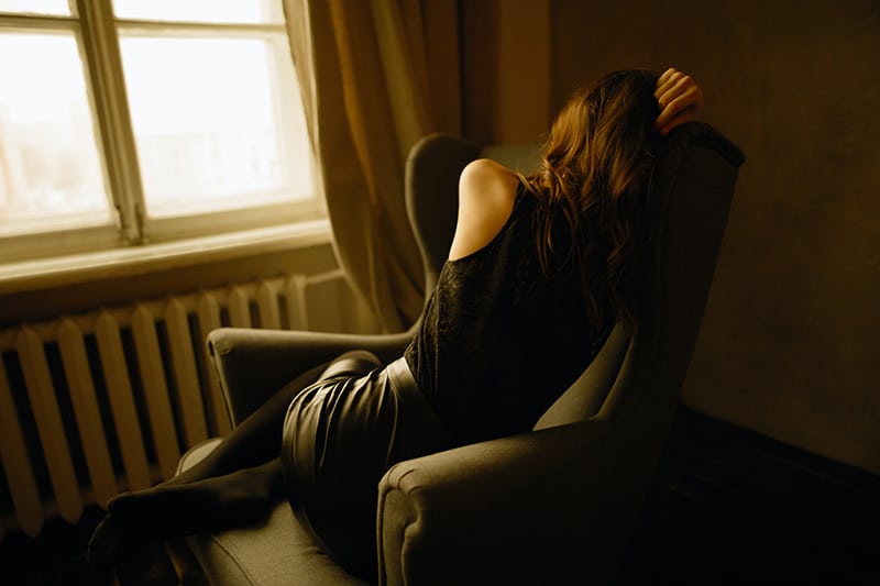 eine traurige Frau, die in einem Sessel neben dem Fenster sitzt