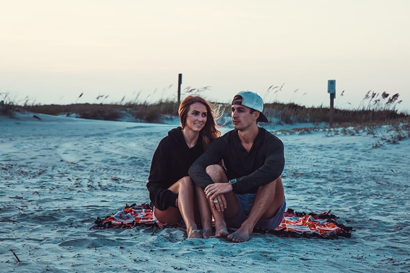monogames Paar, das am Strand während des Sonnenuntergangs sitzt