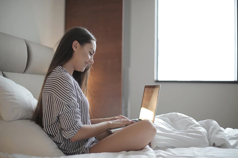 positive junge Frau mit einem Laptop beim Sitzen auf dem Bett