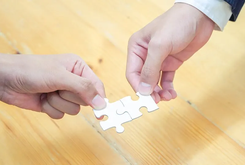 zwei Personen, die Teile eines Puzzles verbinden auf braun unter Holztisch