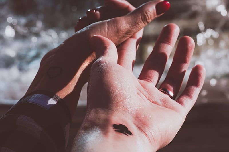 zwei Personen mit einem Tattoo am Handgelenk Händchen haltend