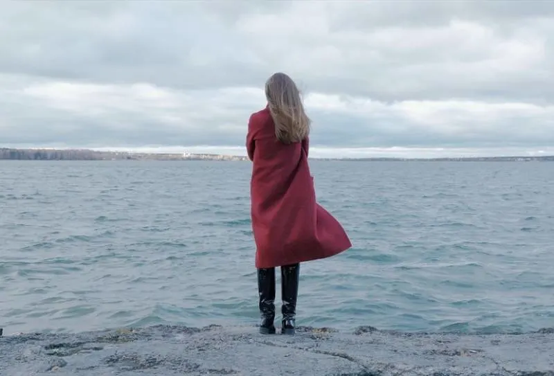 Frau im roten Mantel steht am Strand