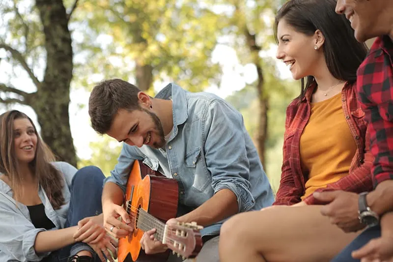 Ein Mann, der Gitarre spielt, während er mit Freunden sitzt